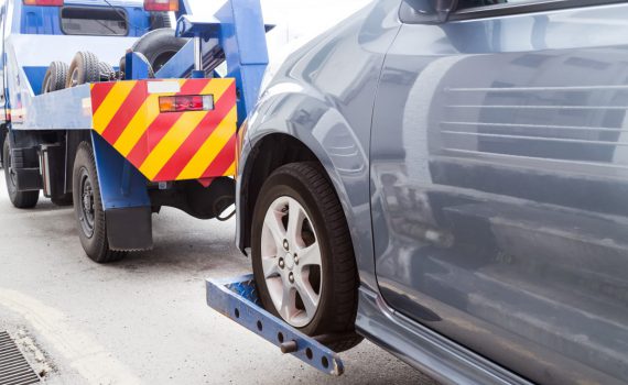 tow truck towing a broken down car on the street PE9HH3A